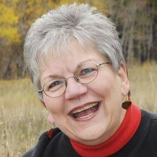 headshot of a smiling woman with short grey hair and wire-rimmed glasses