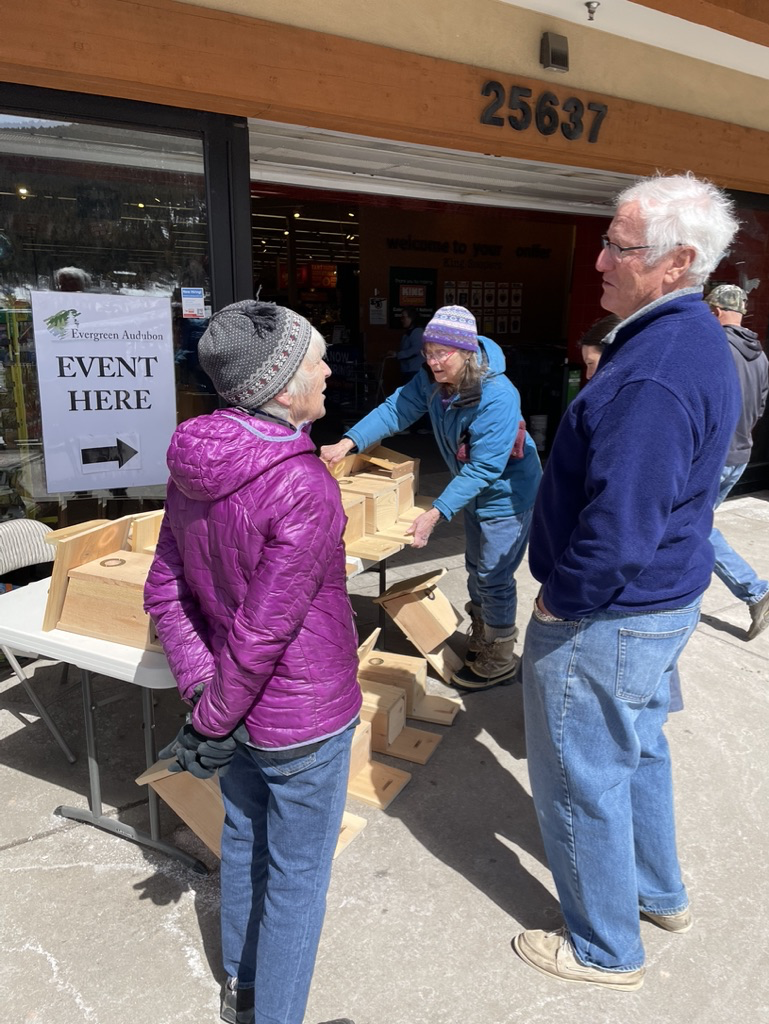 Two women and a man standing in from of a table of nest boxes (birdhouses)