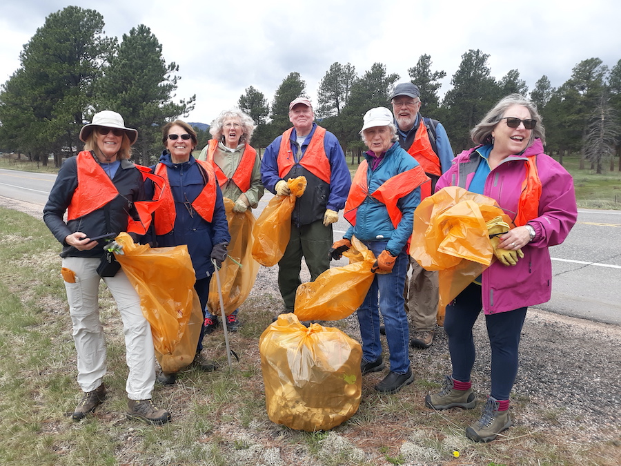 group of people standing around with garbage bags and orange safety vests.