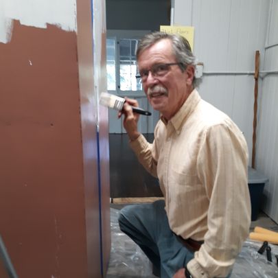man with glasses kneeling as he paints a piece of furniture
