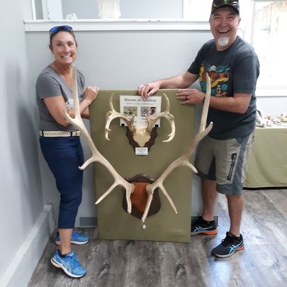 man and a women holding a display of elk and deer antlers