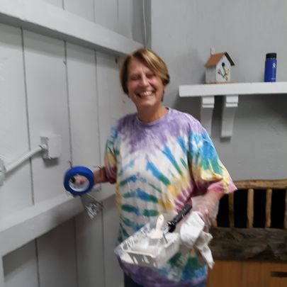 smiling women in a tie-dyed shirt holinding painting supplies