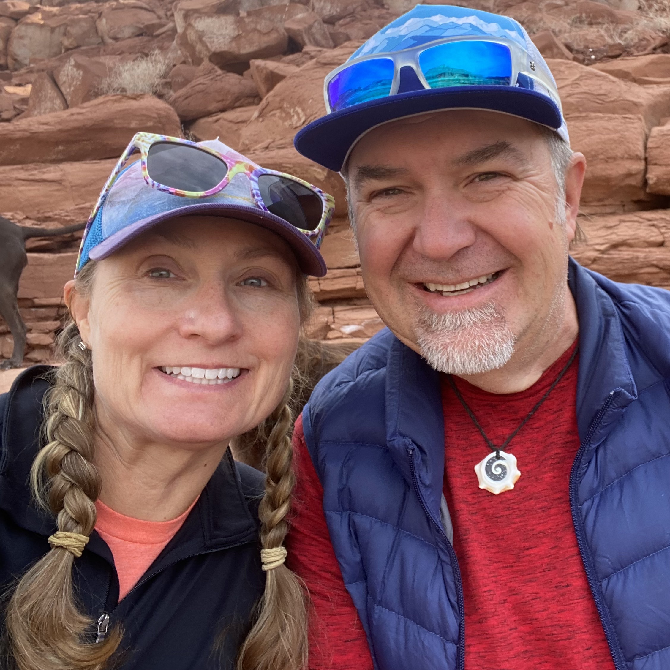 a woman with braids and a hat on the left, and a man with a blue vest and hat on the right
