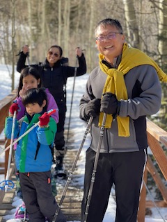Two adults and two children with snowshoes and poles on a wooden bridge with snow