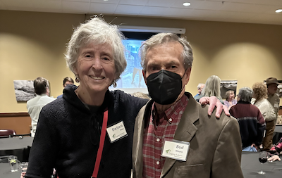 woman on left, man on right with face mask, in a room of other people