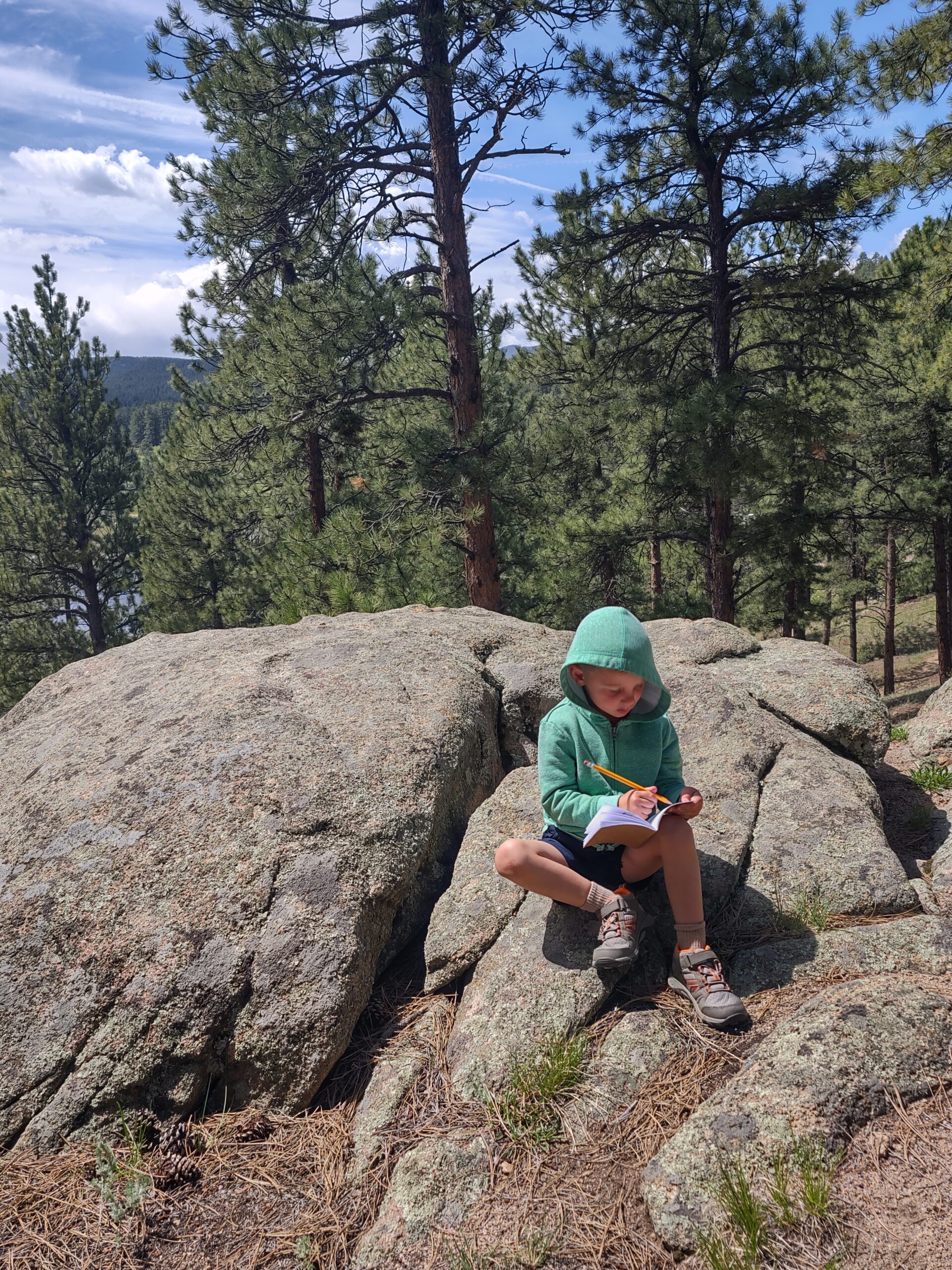 child on boulder writing in a journal