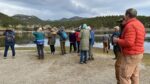 about 20 people next to a lake holding binoculars