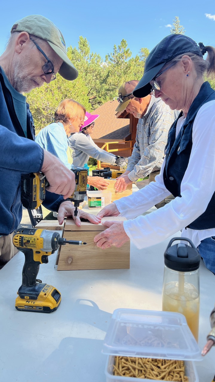 two people making a nestbox on a table in the foreground, and several more in the background outside