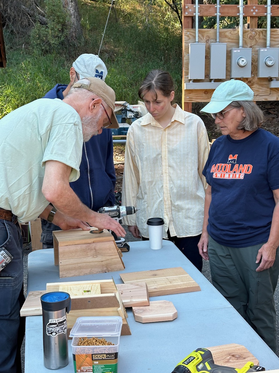 four people making a nestbox on a table outside