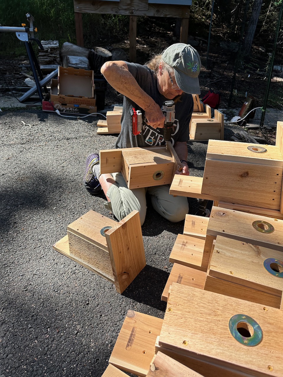 person with drill working with a pile of nestboxes outside on the ground