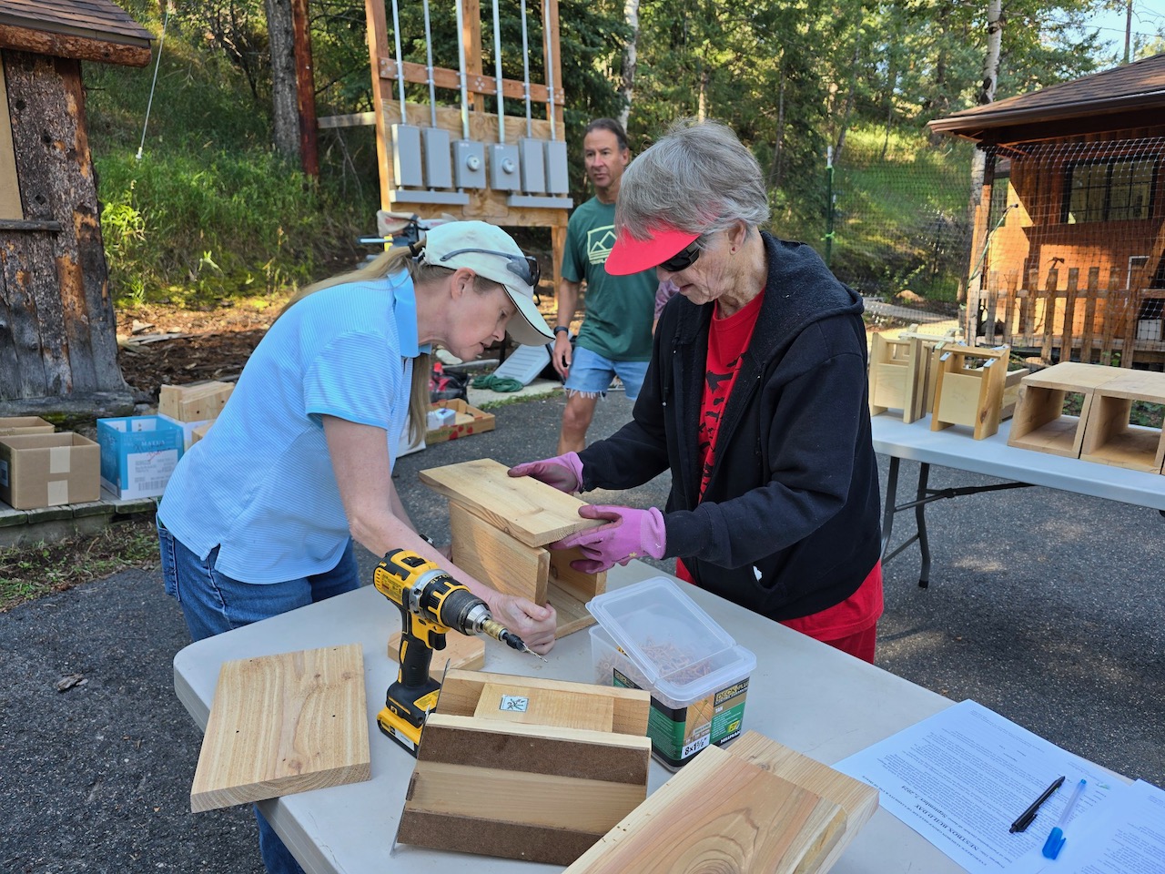 two people putting together a nestbox on a table outside