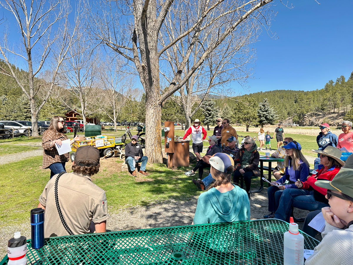 a bunch of people sitting around picnic tables in a meadow