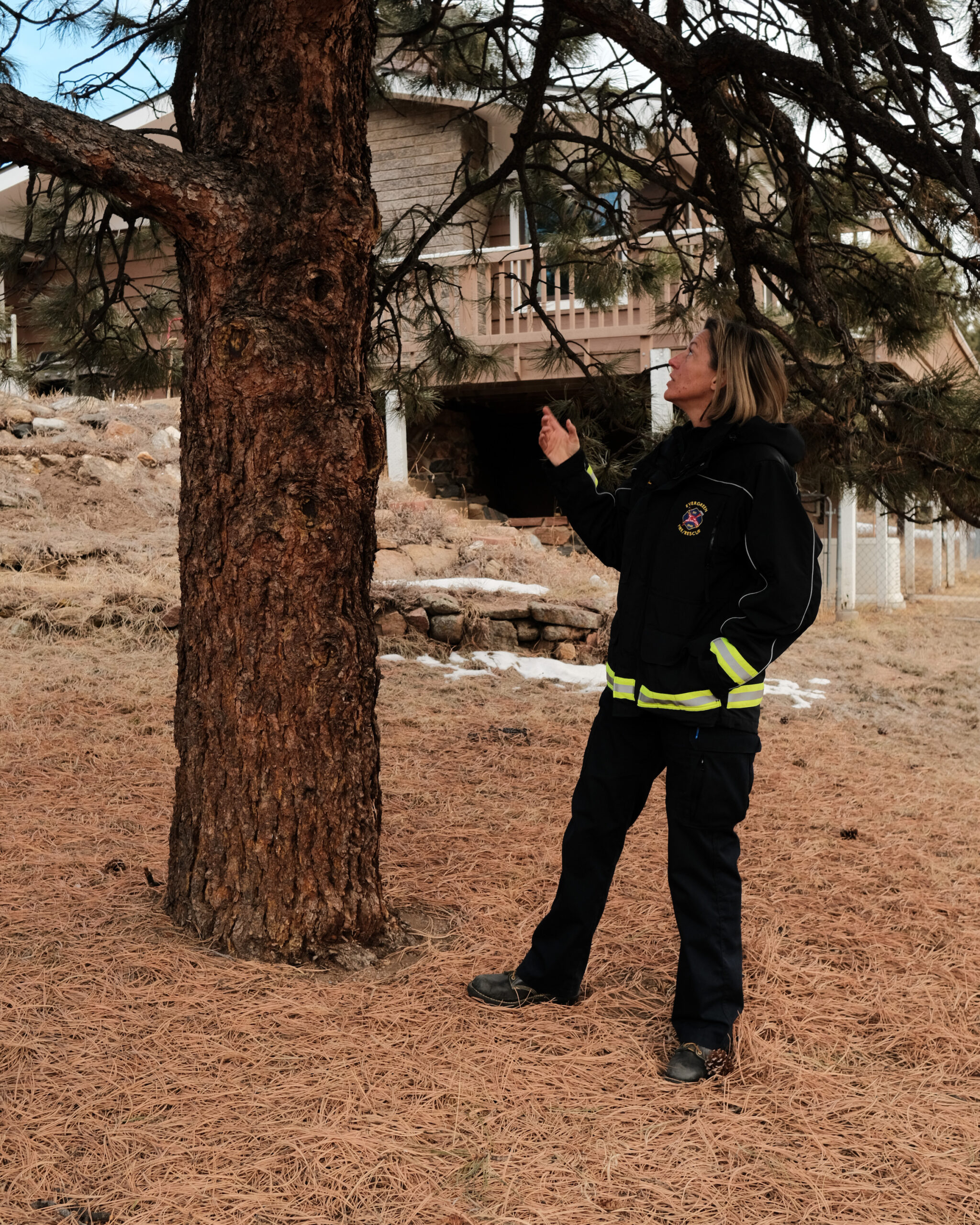 A woman in her black and yellow firewoman uniform gesturing to a ponderosa pine and talking about fire mitigation.