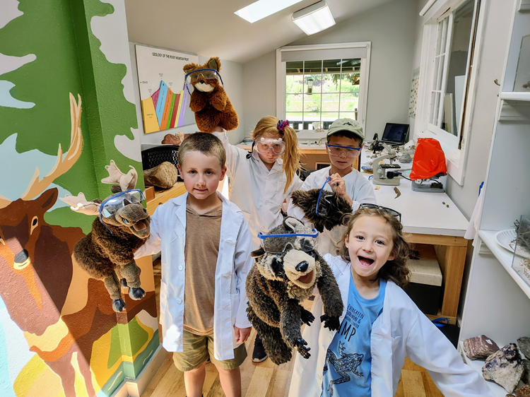 Four kids holding wildlife stuffed animals with science goggles on in the nature center.