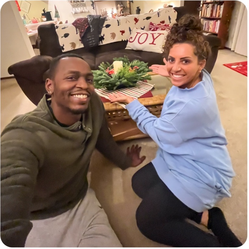 two people sitting on the floor of their living room with their wreath centerpiece on the coffee table behind them