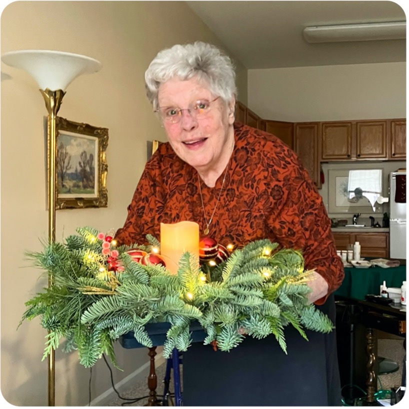 a woman with grayish white hair holding a large wreath centerpiece in her living room