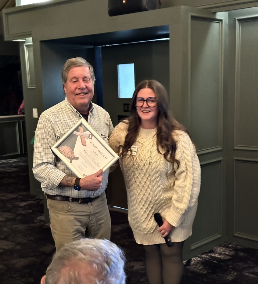man on left holding framed certificate, woman on right