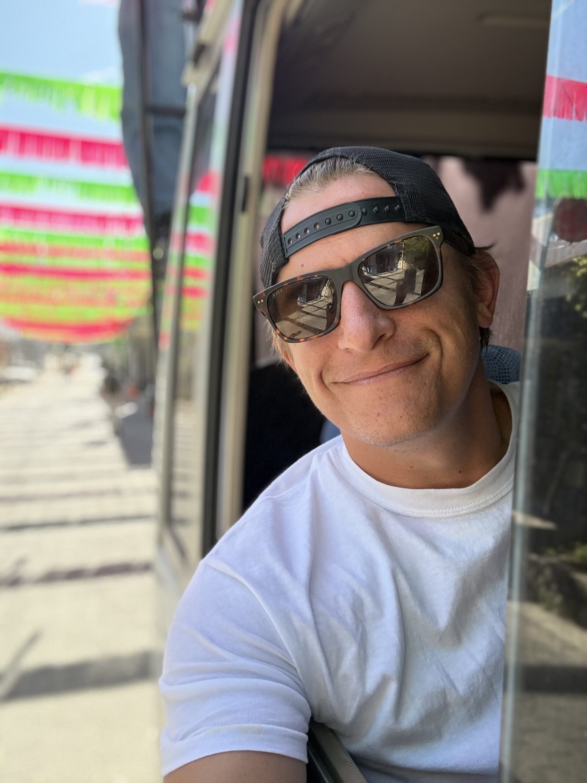 man with sunglasses and a white tshirt hanging out of a window to say hi