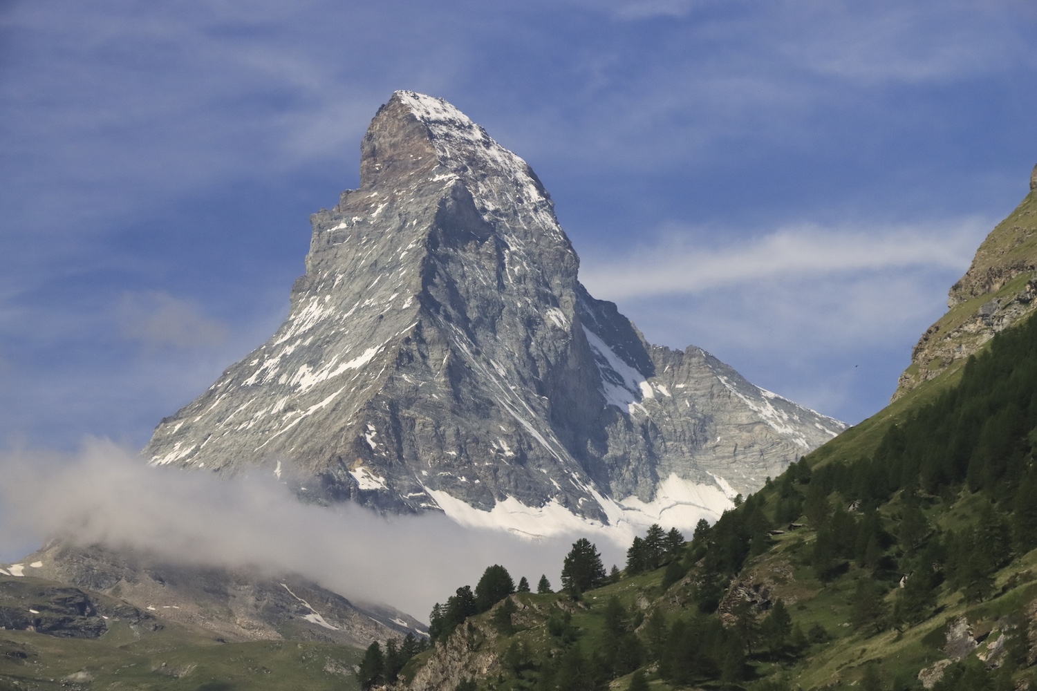 A large sharp, granite mountain with sparse snow against a blue sky with whispy clouds.
